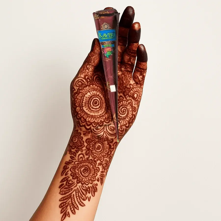 A hand decorated with intricate traditional henna patterns holding a Kaveri Mehndi cone.