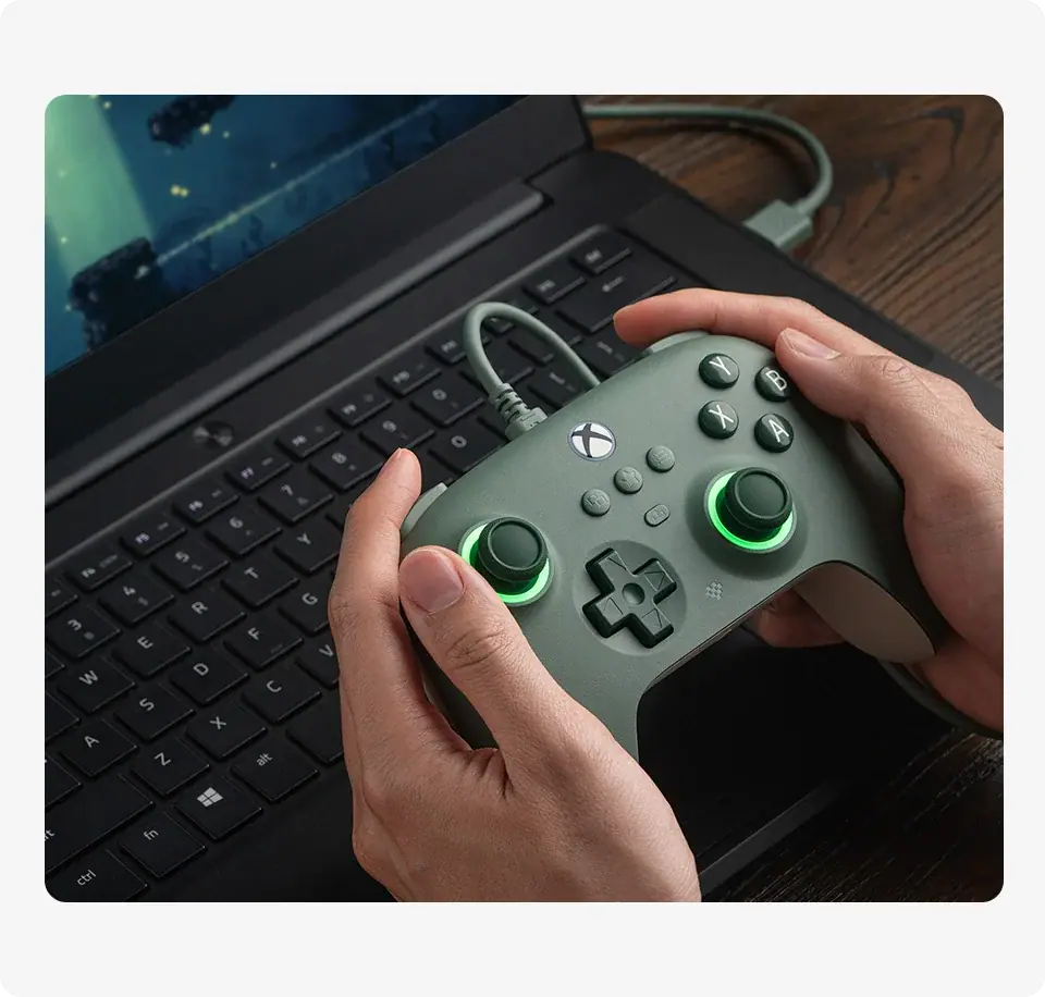 A gamer using the 8BitDo Dark Green wired controller with a gaming laptop.