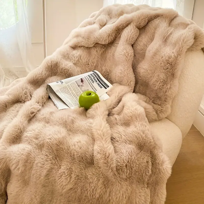 A soft beige faux rabbit fleece throw blanket draped over a cozy white armchair.