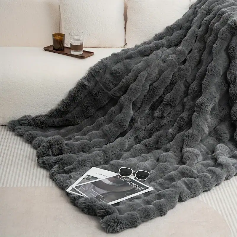 A dark charcoal grey textured fleece blanket on a modern white couch with accessories.