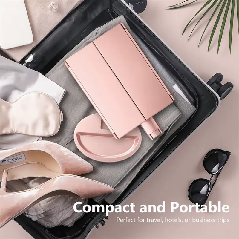 A rose gold LED folding makeup mirror packed neatly in a travel suitcase next to shoes and sunglasses.