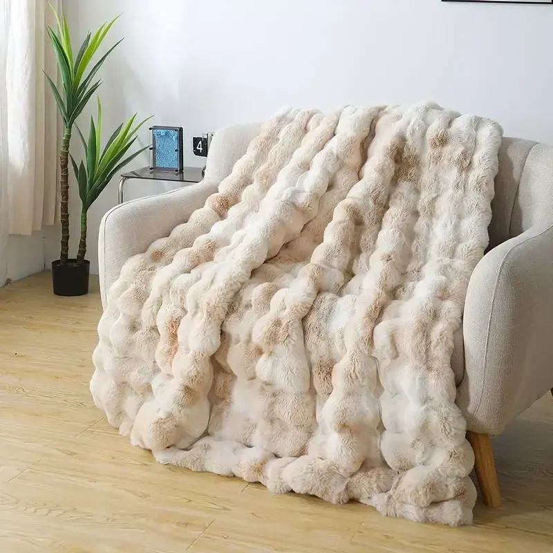 A cream-colored wavy textured fleece blanket displayed on a beige sofa next to a plant.