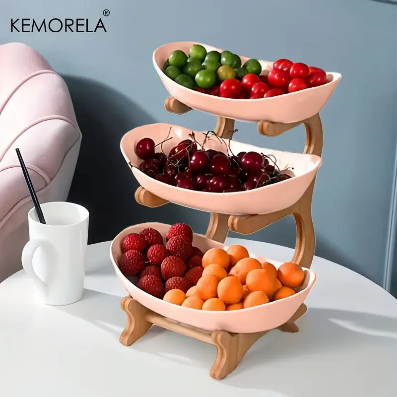 A close-up view of the Kemorela fruit basket review showing three pink plastic tiers filled with fresh cherries, green plums, and apricots.