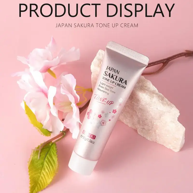 An honest Sakura Essence Cream Review focusing on the LAIKOU Japan Sakura Tone Up Cream tube next to cherry blossoms.