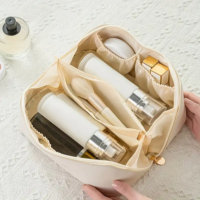 Top-down view of an ivory makeup bag showing how bottles and brushes fit into separate divided sections.