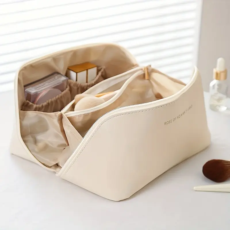 An open cream-colored luxury cosmetic bag showing multiple internal compartments, elastic pockets, and a middle zipper pouch.