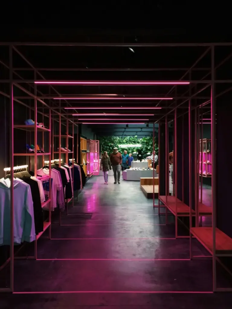 Interior of a modern clothing retail store with vibrant pink neon lights, minimalist apparel racks, and a stylish shopping ambiance.