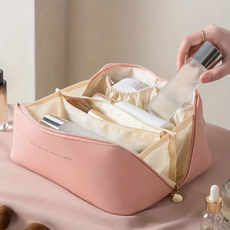A hand placing a skincare bottle into a pink leather makeup bag with gold zipper detailing.