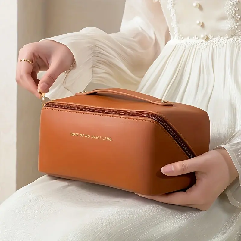 A person holding a tan leather makeup organizer by its sturdy top handle.