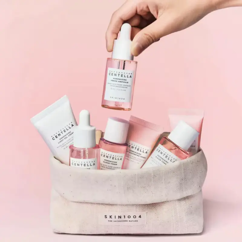 A hand holding the SKIN1004 Madagascar Centella Poremizing Fresh Ampoule bottle over a fabric basket of skincare.