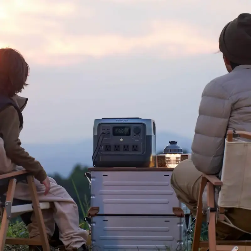 Two campers relaxing outdoors at sunset using the EcoFlow River Portable Power station for camp lighting.