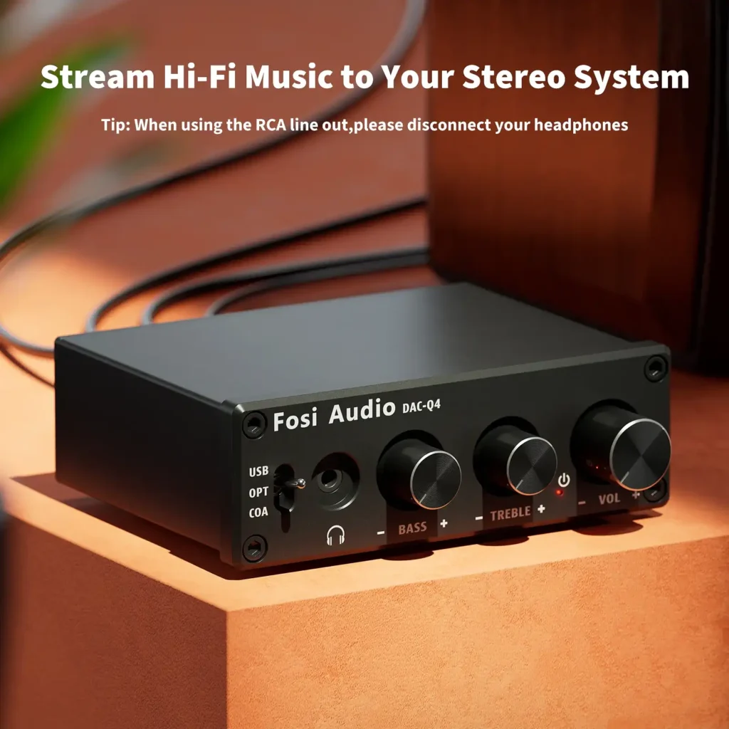 Compact mini stereo gaming DAC and headphone amplifier resting on a desk next to a wooden speaker system.