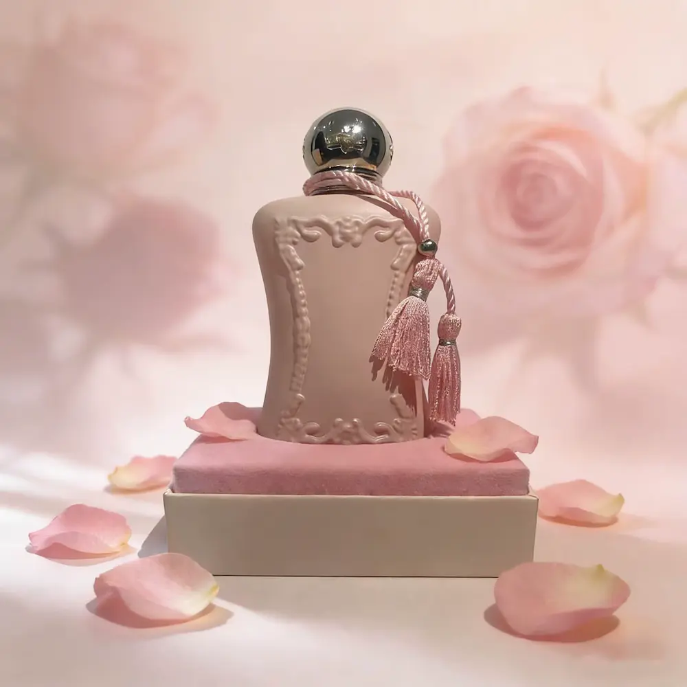 The elegant pink bottle of Delina Eau de Parfum displayed beautifully on a velvet stand with rose petals.