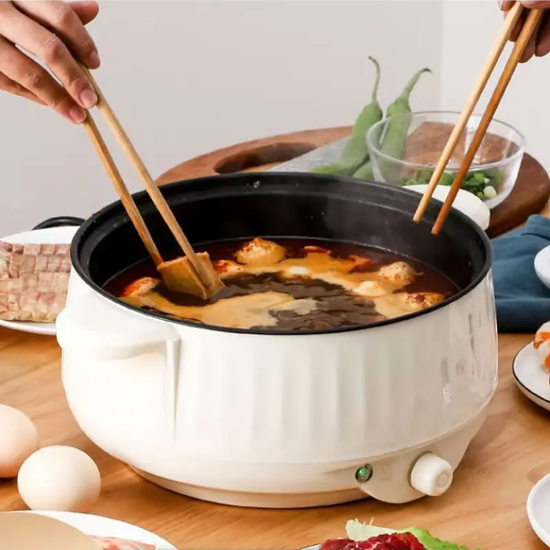 Electric cooking pot preparing a hot-pot-style meal with vegetables and meat.